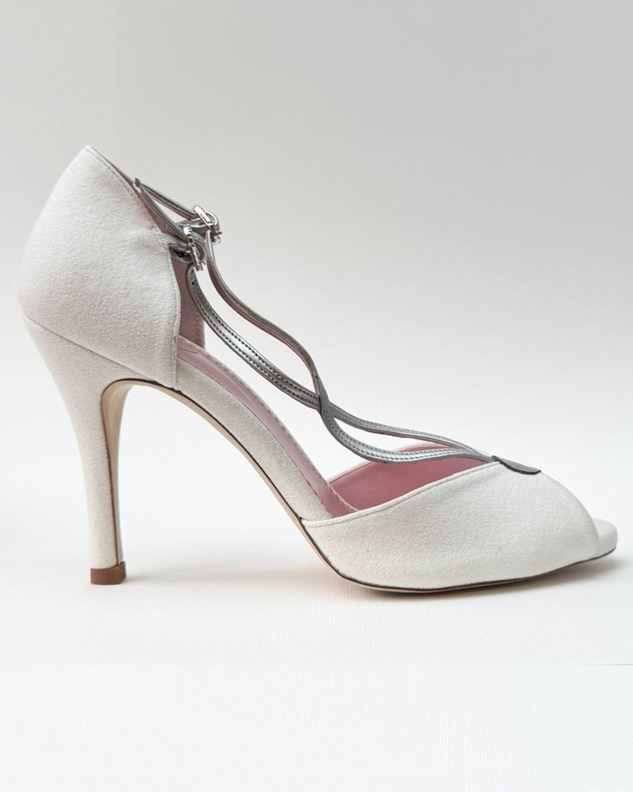 Elegant white peep-toe heels with a delicate crisscross strap design. The shoes feature a sleek silhouette and a stiletto heel, positioned against a clean, light background. The angle showcases the side profile, highlighting the shoe's refined shape and detailing. image