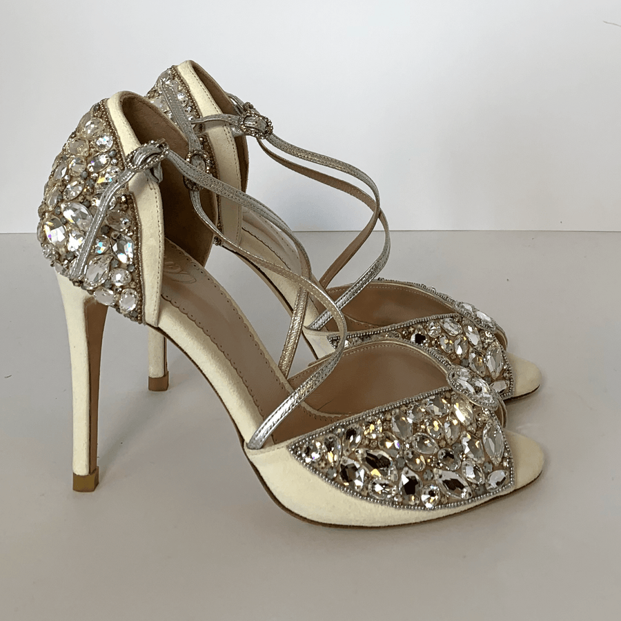 Elegant open-toe heels featuring a sparkling crystal embellishment on the upper. The shoes have a delicate ankle strap and are set against a clean white background. The angle showcases the intricate detailing and the slender stiletto heel, which appears to be high. The material looks like a combination of suede and leather. image