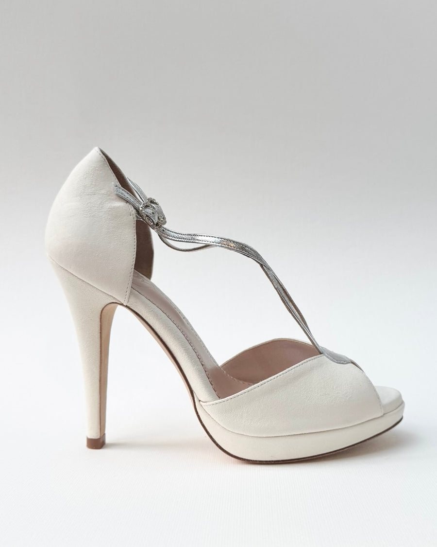 Elegant white high heels featuring a peep-toe design and a delicate ankle strap. The shoes are made of leather and have a sleek, modern silhouette. The image is taken from a side angle against a soft, neutral background, highlighting the shoe's height and stylish features. image