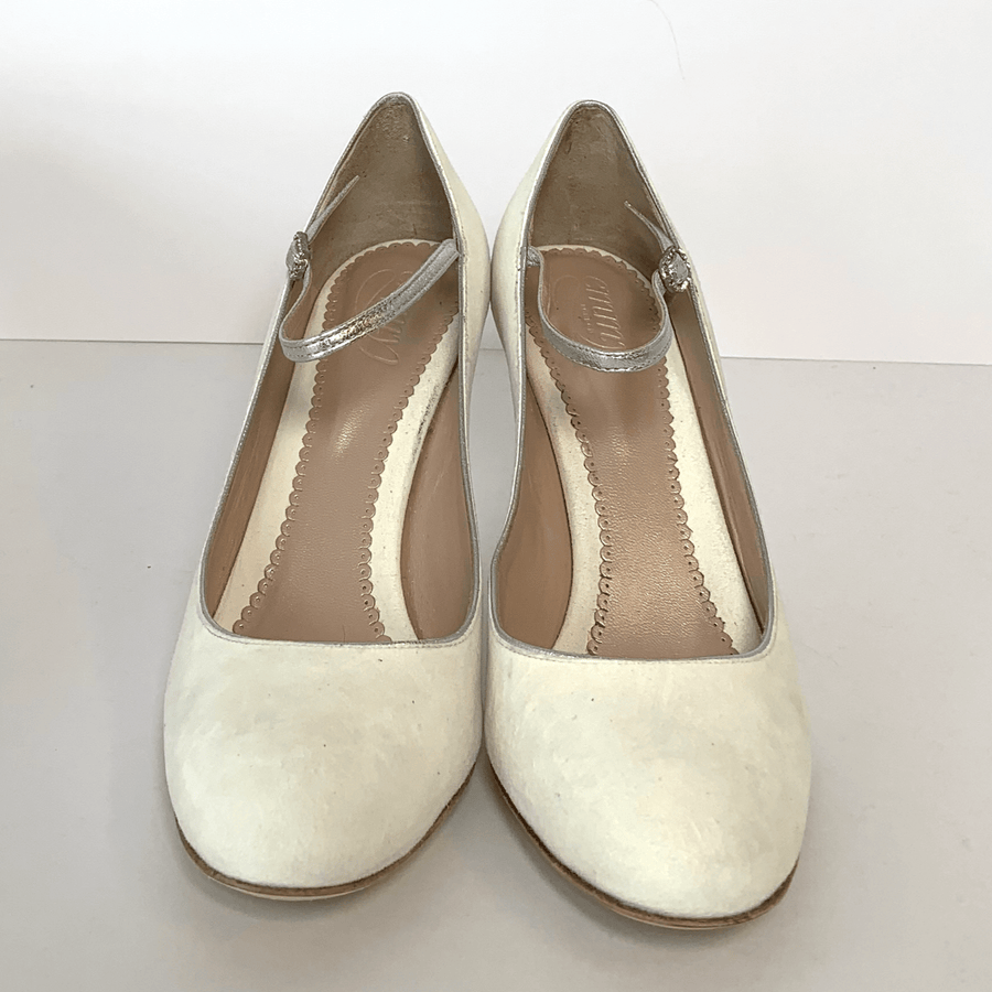 White suede heels with a rounded toe and a delicate ankle strap. The shoes are displayed on a light background, showcasing their elegant design. The angle captures both shoes side by side, emphasizing their smooth texture and clean lines. image
