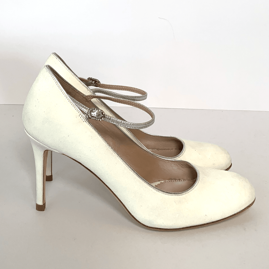 White suede heels with a slender ankle strap, set against a plain white background. The shoes feature a rounded toe and a high stiletto heel, showcasing a side angle view. image