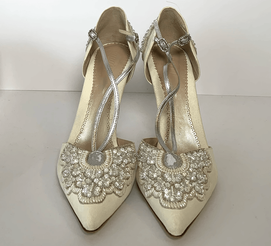 Elegant ivory heels featuring intricate beading and embroidery on the pointed toe. The shoes have delicate silver straps that crisscross over the instep. They are displayed against a plain white background, showcasing their detailed design. The heel height appears to be mid. image