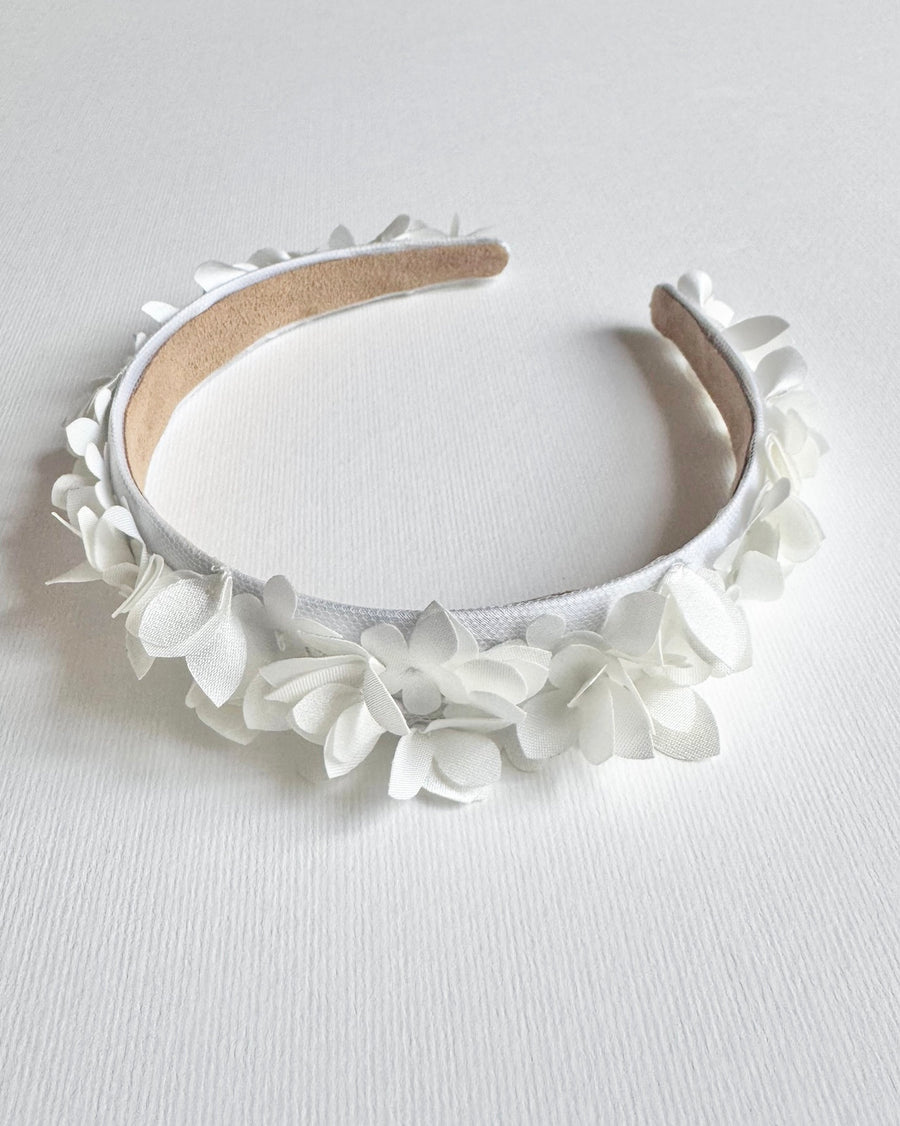 White floral headband made of fabric flowers, displayed on a plain white background. The headband has a smooth finish and a soft inner lining for comfort. image