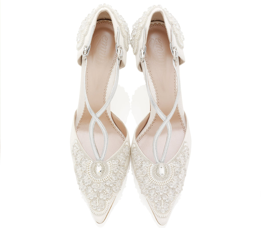 Elegant white pointed-toe heels adorned with intricate beading and embroidery. The shoes feature a delicate ankle strap and a low heel. The image is taken from a top-down angle against a clean, white background, showcasing the detailed craftsmanship of the shoes. image