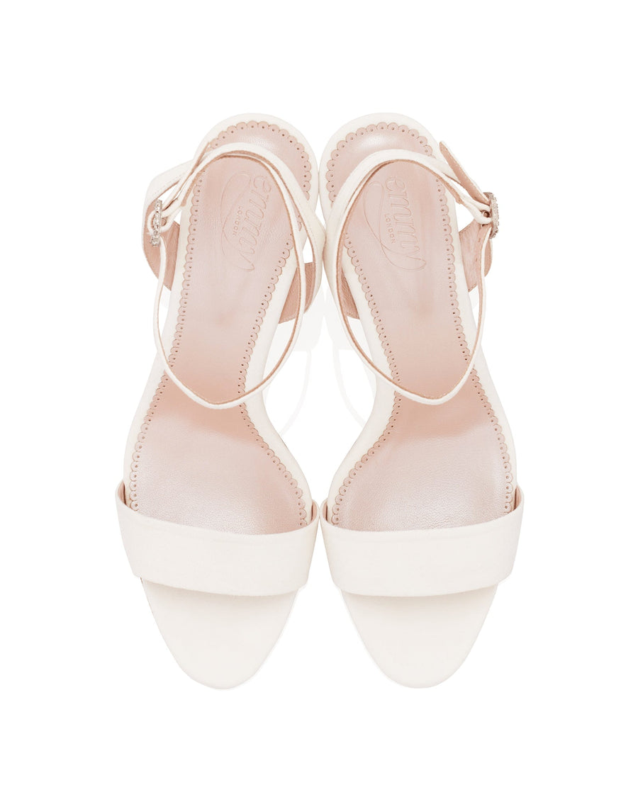 White leather sandals with a minimalist design, featuring a wide front strap and a delicate ankle strap. The image is taken from a top-down angle, showcasing the smooth texture of the leather. The background is plain white, emphasizing the simplicity and elegance of the shoes. image