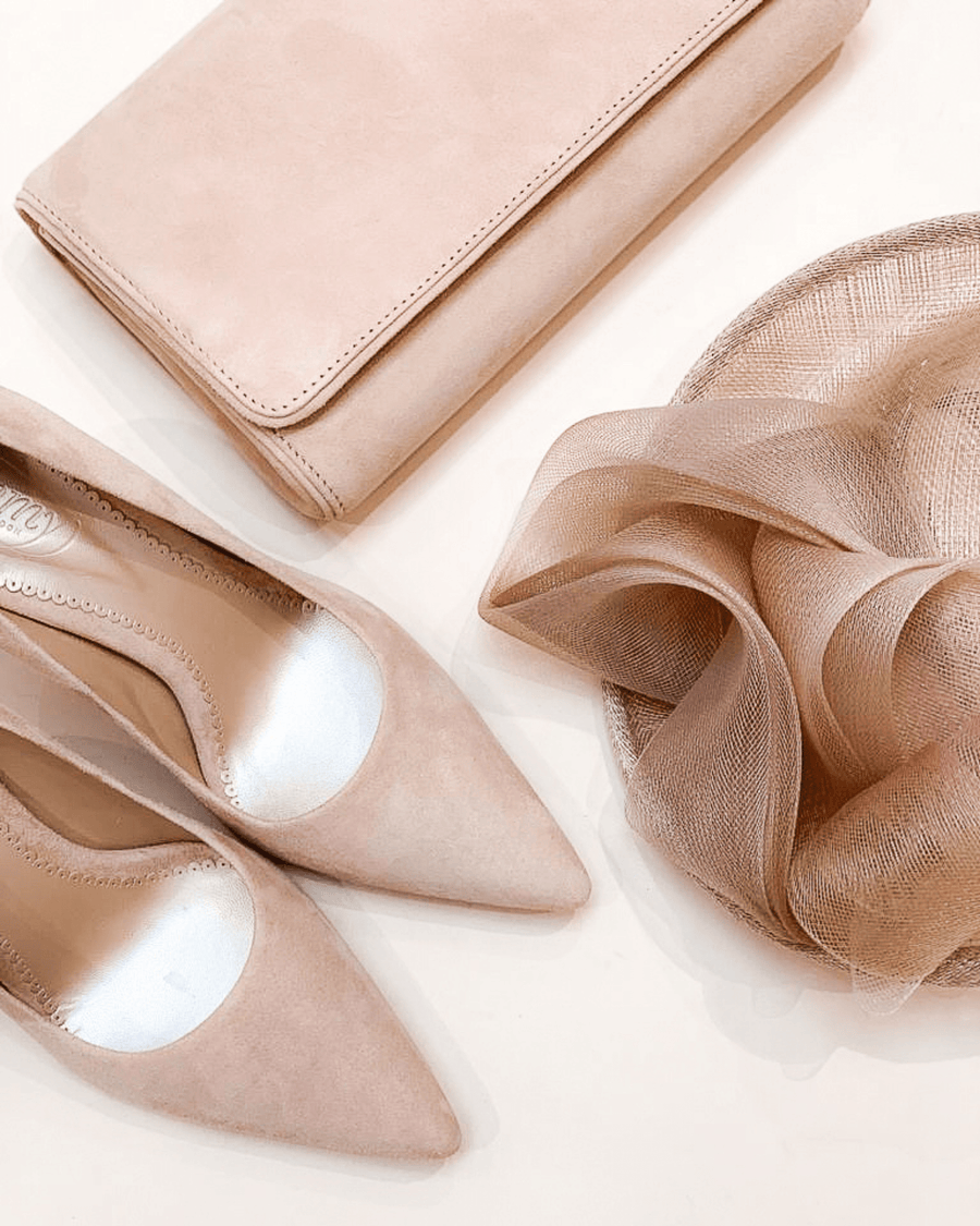 Elegant blush suede heels with a pointed toe are displayed alongside a matching clutch and a delicate, sheer fabric. The shoes are positioned at an angle, showcasing their sleek design. The background is a soft, neutral tone, enhancing the overall sophisticated look. image