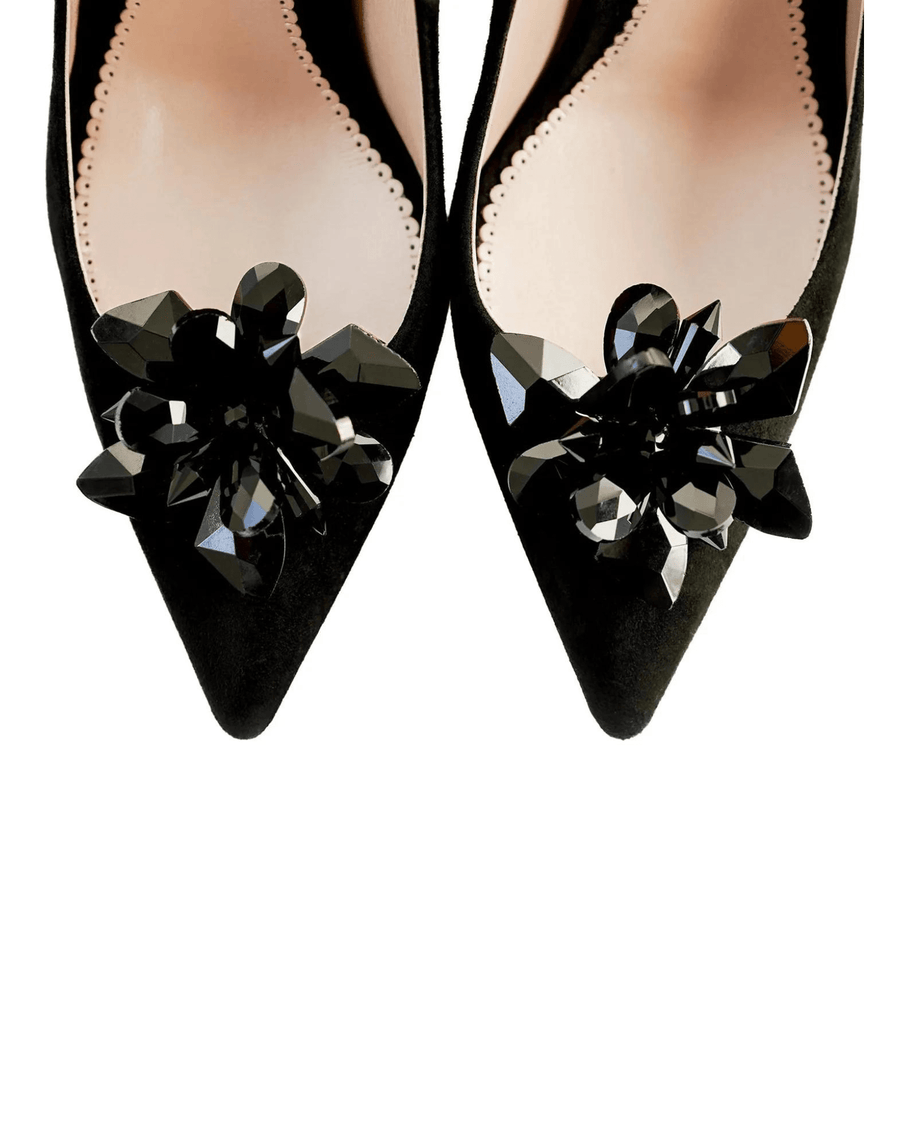Black suede heels featuring a pointed toe design adorned with large black crystal embellishments. The shoes are positioned against a white background, showcasing their elegant silhouette. The angle captures the front view, highlighting the intricate detailing of the floral accents. image