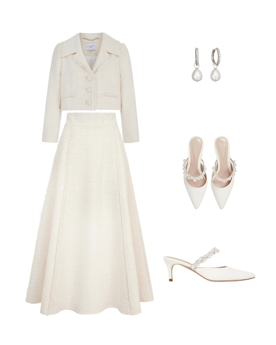 Elegant white heels with a pointed toe and a delicate embellishment on the strap, set against a clean, white background. The shoes are styled alongside a matching tweed skirt and jacket, with pearl earrings completing the sophisticated look. The angle showcases the shoes prominently, highlighting their chic design. image