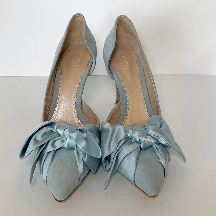 Light blue suede heels with a pointed toe and large satin bows at the front. The shoes are displayed on a plain white background, showcasing their elegant design. The angle of the image captures the shoes from the front, emphasizing the bows and the sleek silhouette. image