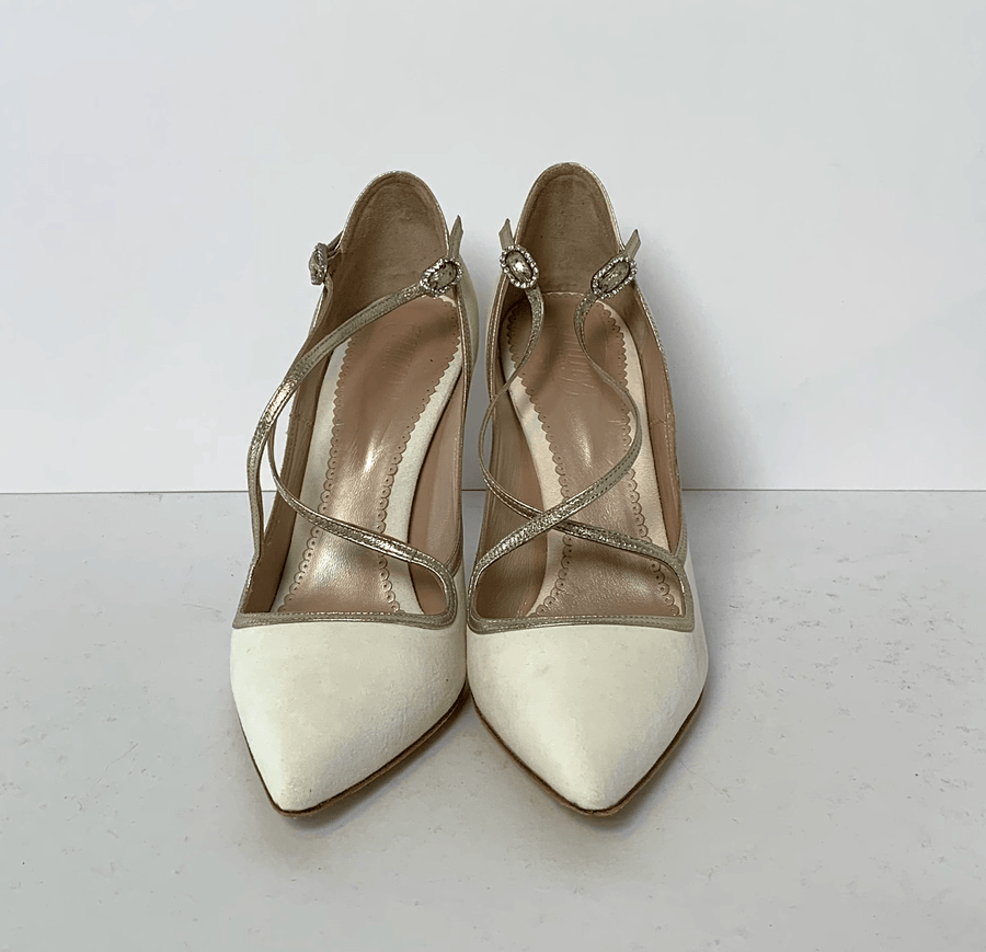 White pointed-toe heels with crisscross straps and decorative embellishments at the ankle. The shoes are displayed against a plain white background, showcasing their elegant design. The angle captures the front view, highlighting the sharp silhouette and the delicate detailing of the straps. image