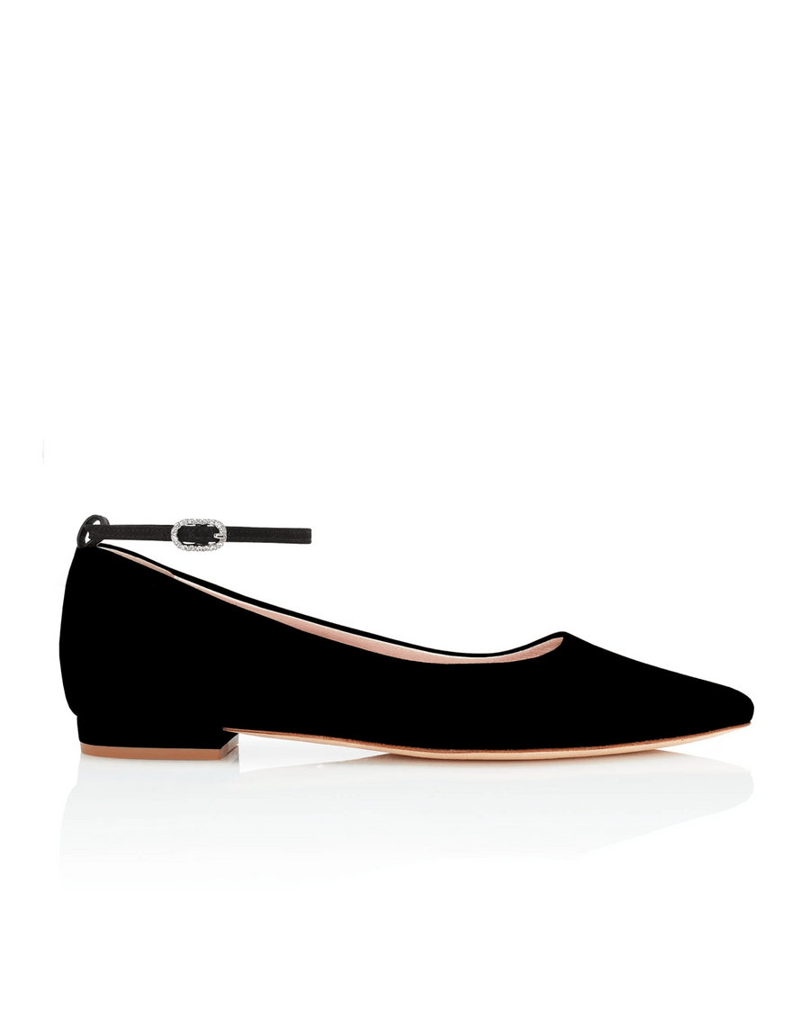 Black suede flats with a low heel, featuring a delicate ankle strap. The shoe is positioned against a white background, showcasing its sleek design from a side angle. image