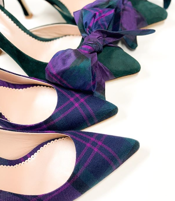 Elegant heels in a close-up arrangement featuring a pair of green suede pumps with a bow detail and a pair of purple tweed pumps with a plaid pattern. The background is a soft white, highlighting the shoes' textures and colors. The image captures the shoes from a top-down angle, showcasing their pointed toes and stylish design. image