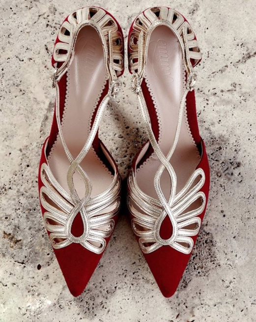 Red suede heels with intricate silver detailing, featuring a pointed toe and a mid-height heel. The shoes are displayed from a top-down angle on a textured, light-colored surface, showcasing their elegant design. image
