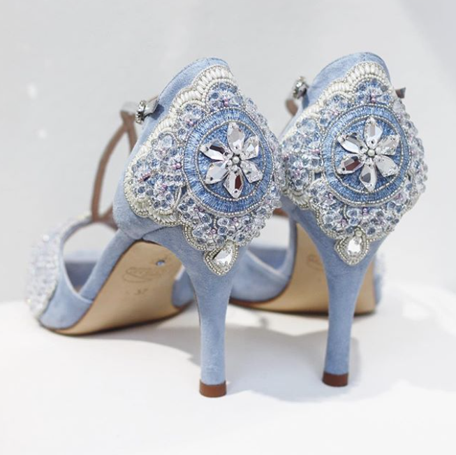 Elegant blue suede heels featuring intricate embellishments on the back, showcasing a high heel design. The image is taken from a rear angle against a light background, highlighting the detailed craftsmanship. image